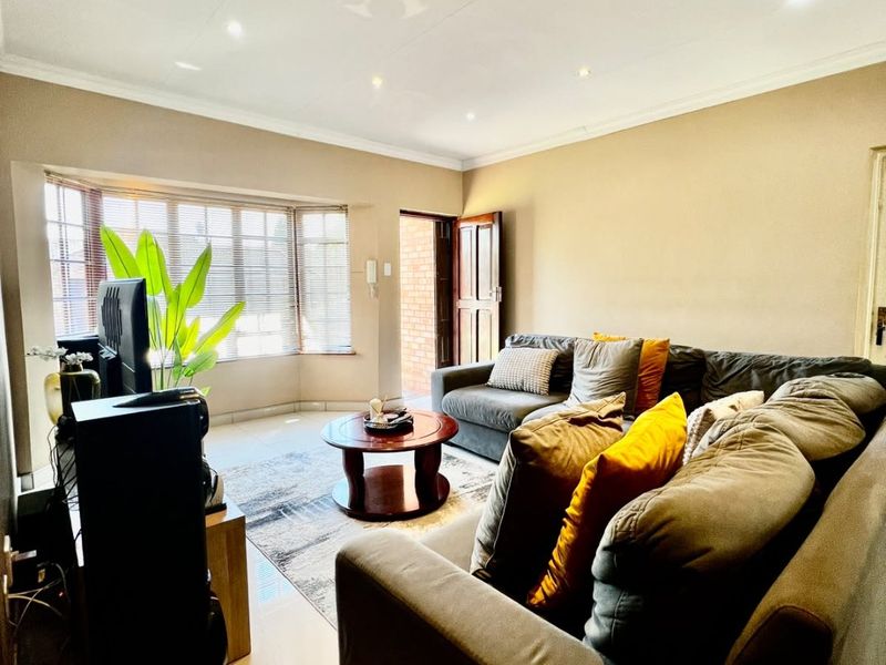 A well-lit living room featuring tiled flooring, recessed downlights, and a bay window that provides natural light.