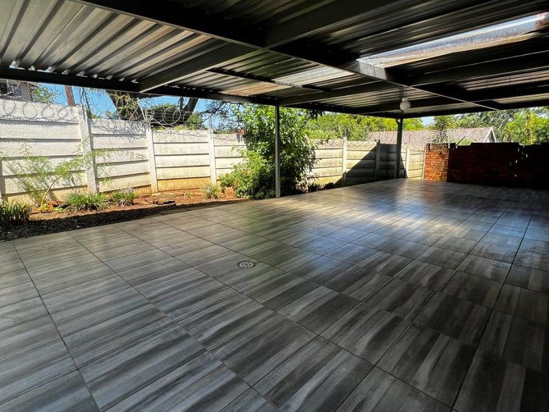 A spacious, covered outdoor patio area featuring modern wood-look floor tiles, a corrugated metal roof, and secure perimeter walling.