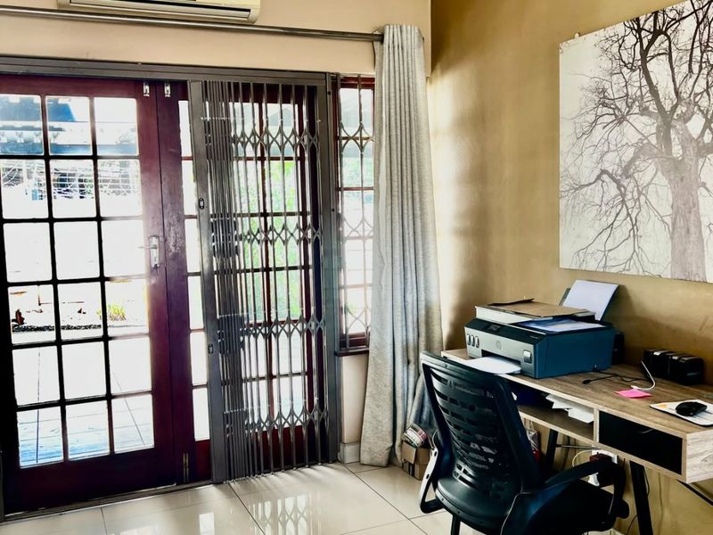 A functional home office space featuring tiled flooring, recessed lighting, and direct access to the outdoors via a sliding glass door with security gate.
