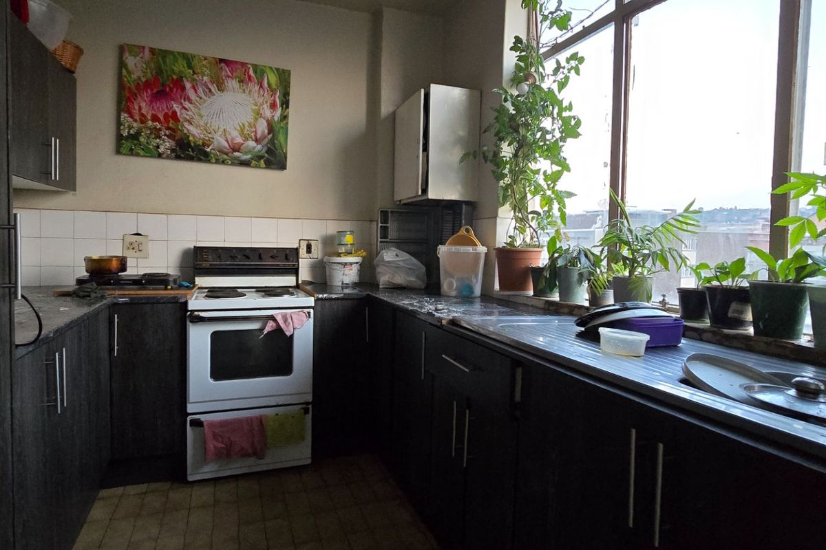 A functional kitchen featuring dark wood cabinetry, laminate countertops, a stainless steel sink, and a freestanding stove, illuminated by a large window.