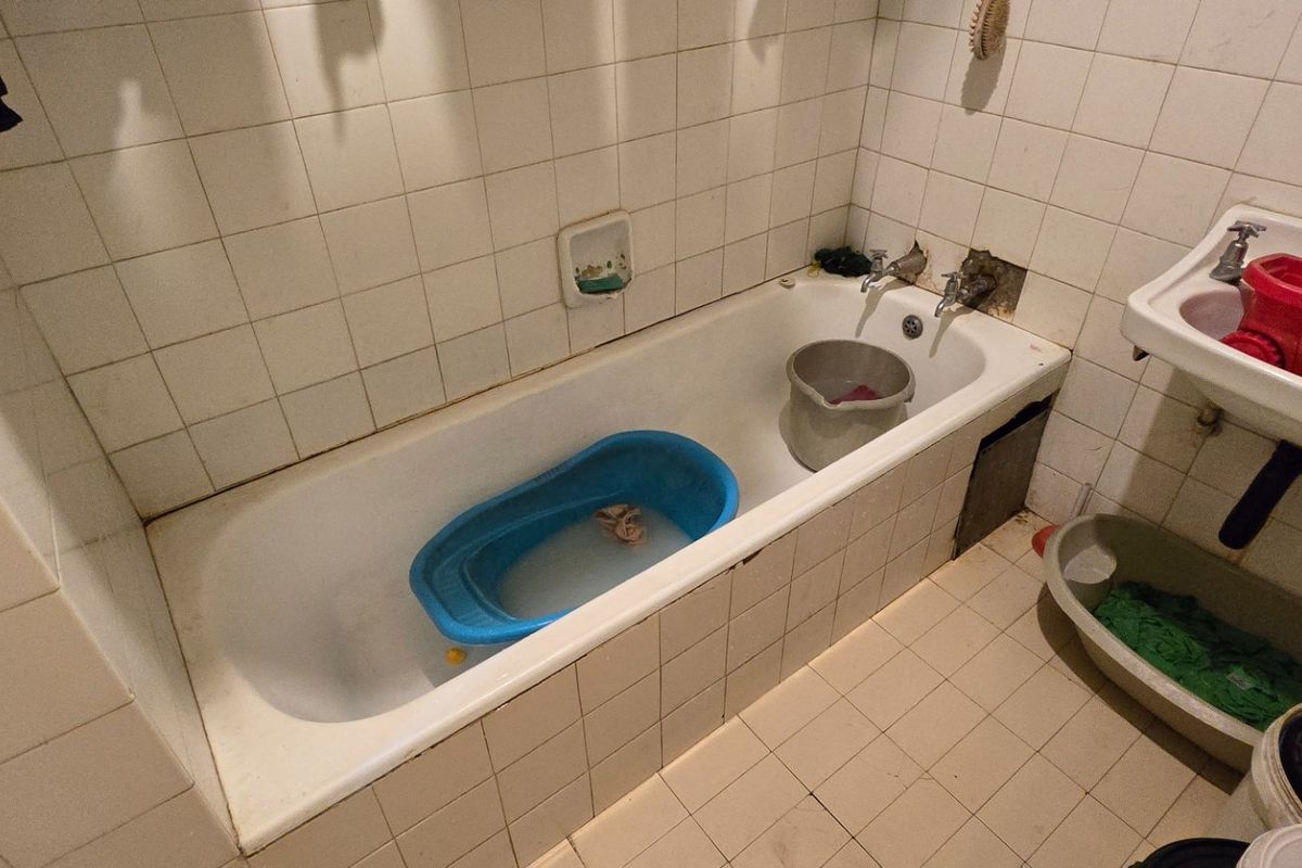 A dated bathroom featuring a standard bathtub and wall-mounted basin with tiled finishes, requiring maintenance and cosmetic updates to improve its condition.