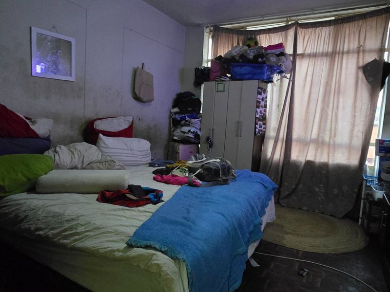 A bedroom featuring a large window and built-in wardrobe, currently showing signs of wear and requiring cosmetic updates to the wall finishes.
