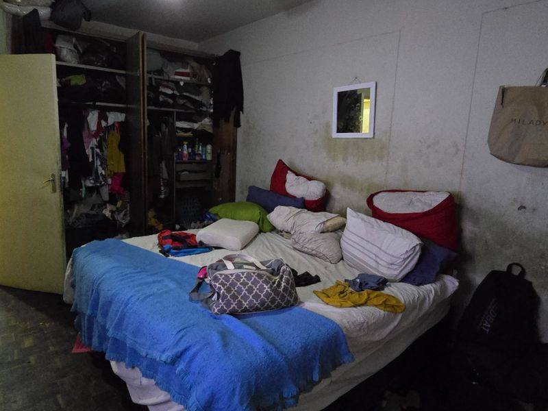 A bedroom featuring a built-in wardrobe, currently showing significant wall staining and surface wear requiring maintenance and cosmetic updates.