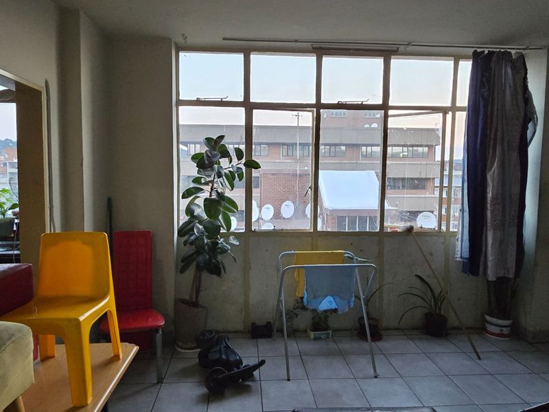 A living area featuring tiled flooring and a large window with natural light, offering potential for modernization and improved layout.