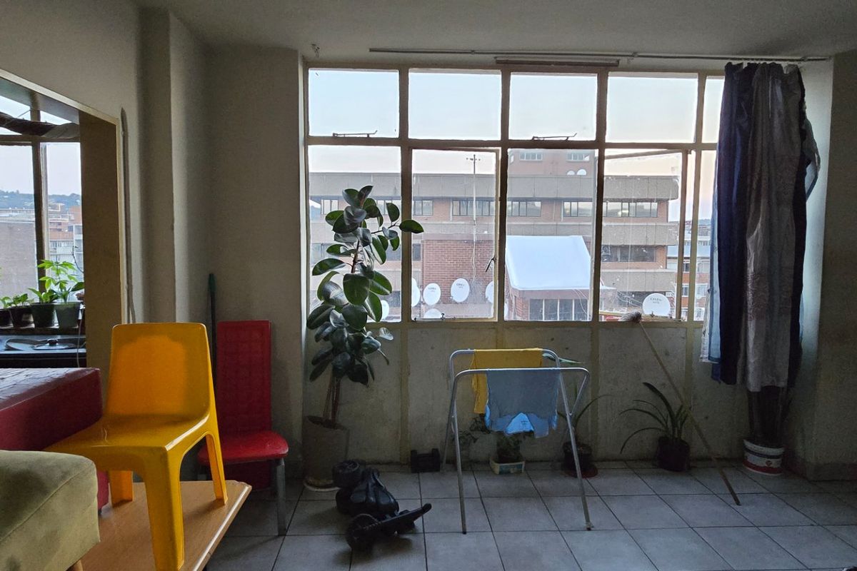 A living area featuring large multi-pane windows providing natural light and tiled flooring, currently in need of cosmetic updates and maintenance.