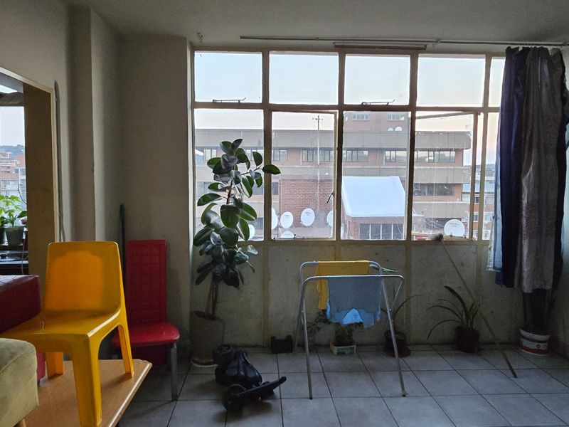 A living area featuring large multi-pane windows providing natural light and tiled flooring, currently in need of cosmetic updates and maintenance.