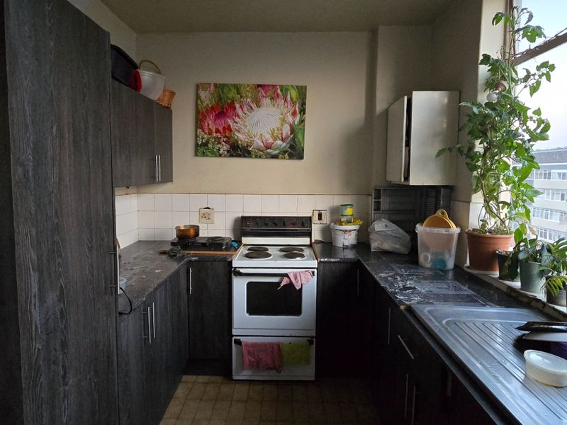 A compact kitchen featuring dark wood cabinetry, a freestanding electric stove, and a stainless steel sink, illuminated by a large window.