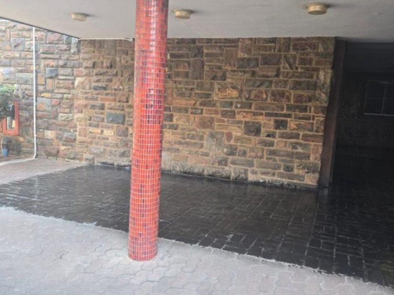 Covered entrance area featuring a distinctive mosaic-tiled column and natural stone wall cladding with paved driveway access.