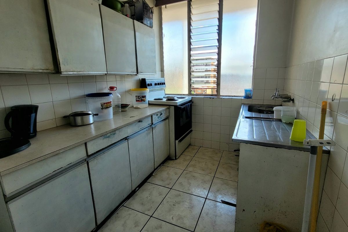 A dated kitchen featuring original cabinetry, tiled surfaces, and a stainless steel sink, requiring modernization to improve functionality and aesthetic appeal.