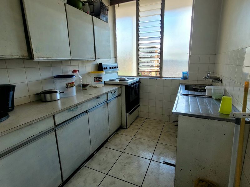 A dated kitchen featuring original cabinetry, tiled surfaces, and a stainless steel sink, requiring modernization to improve functionality and aesthetic appeal.