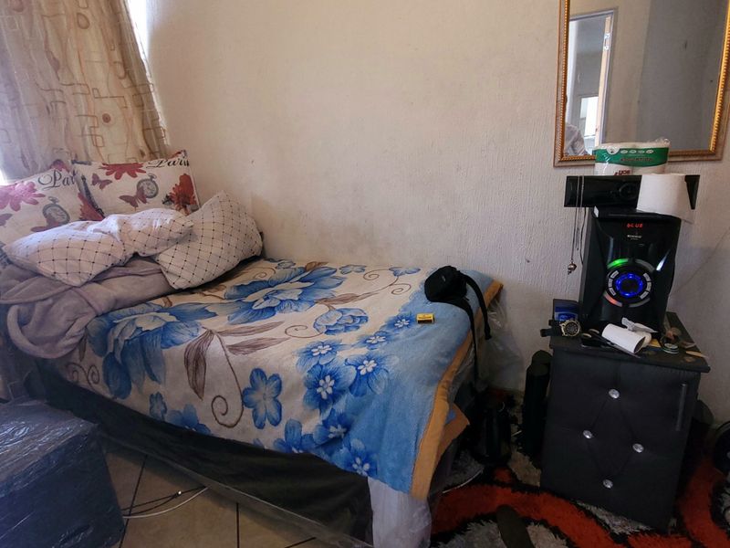 A compact bedroom featuring tiled flooring and a wall-mounted mirror, requiring cosmetic updates to the wall finishes.