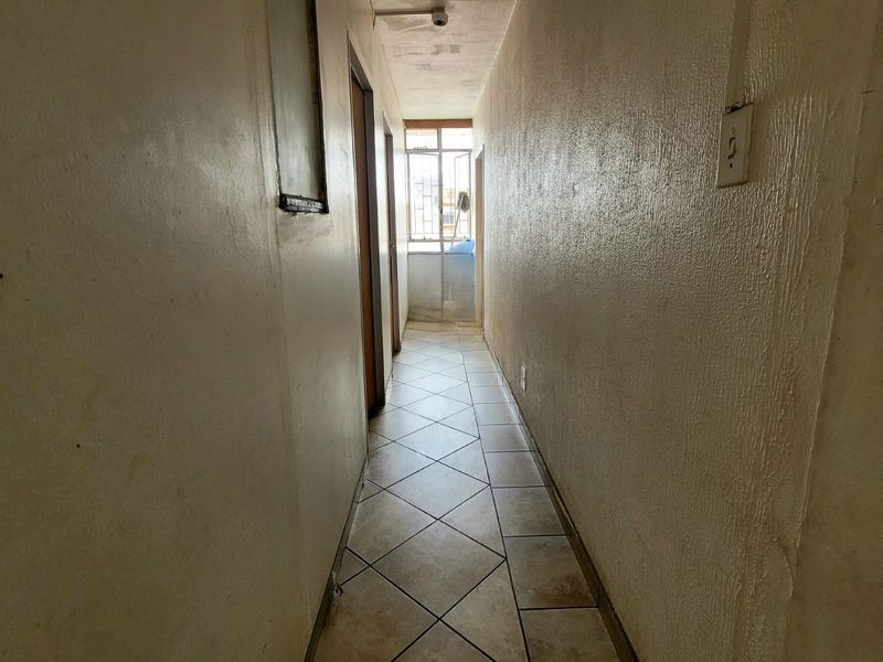 A narrow hallway featuring tiled flooring and access to adjacent rooms, currently in need of cosmetic refurbishment and wall repairs.