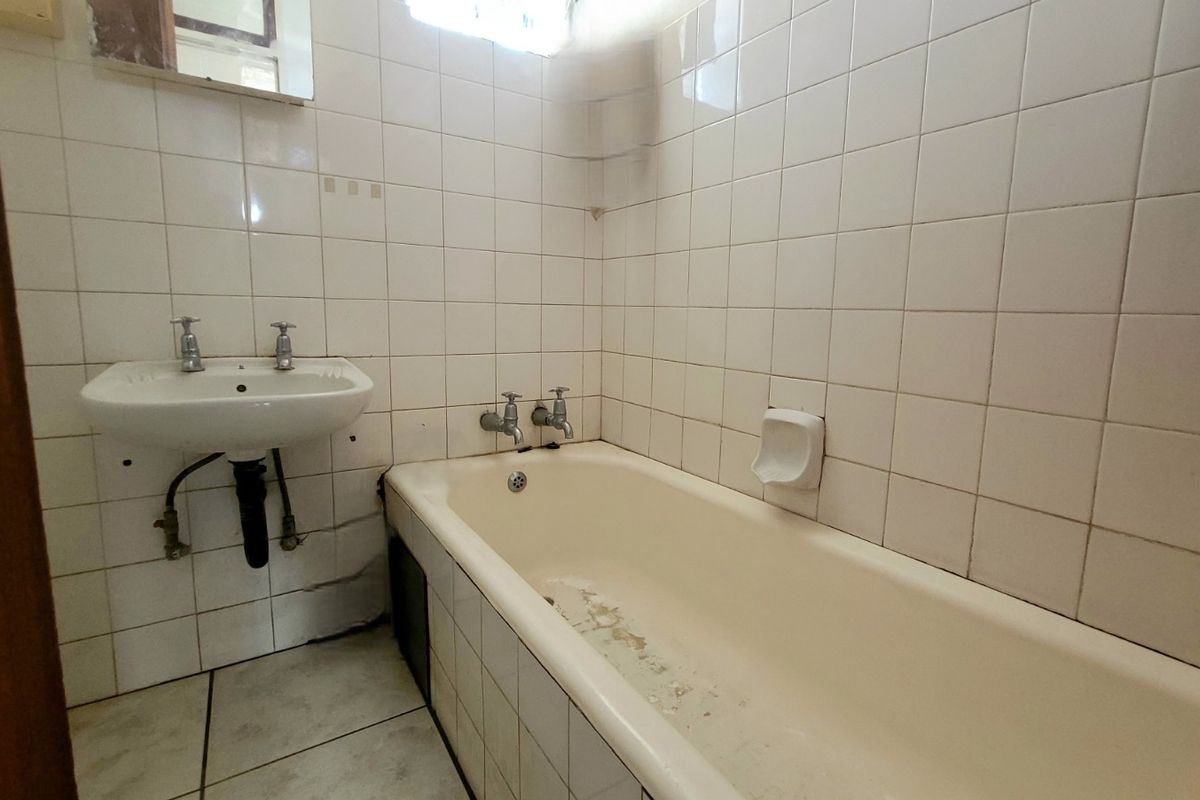 A dated bathroom featuring a built-in bathtub and wall-mounted basin, requiring renovation to update the worn finishes and fixtures.