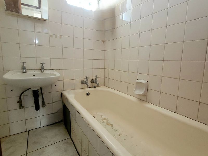 A dated bathroom featuring a built-in bathtub and wall-mounted basin, requiring renovation to update the worn finishes and fixtures.