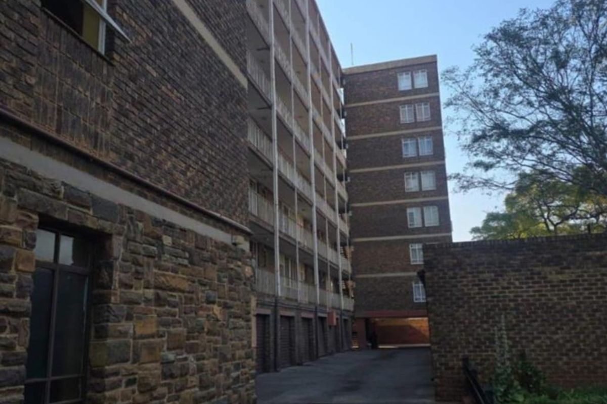 Exterior view of a multi-story apartment building featuring brick and stone facade, paved driveway, and balcony access along the rear elevation.