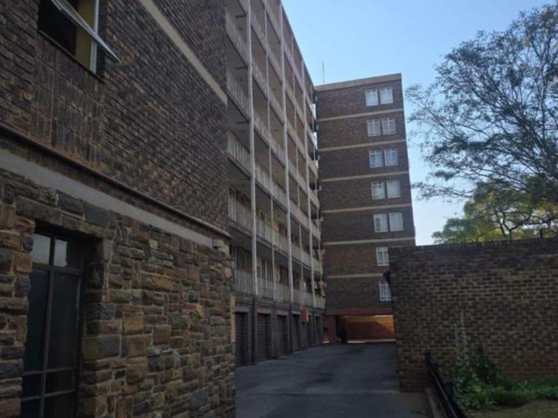 Exterior view of a multi-story apartment building featuring brick and stone facade, paved driveway, and balcony access along the rear elevation.