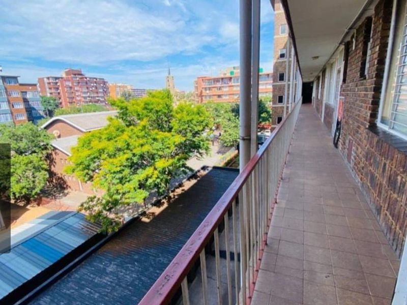 An open-air apartment balcony featuring tiled flooring, a metal safety railing, and views over the surrounding residential complex.
