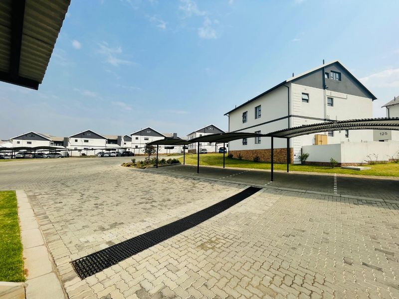A well-maintained townhouse complex exterior featuring paved driveways, covered carport parking, and neat landscaping.
