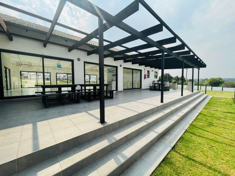A modern clubhouse patio featuring a large pergola, tiled flooring, and expansive sliding glass doors, providing a clean and well-maintained outdoor entertainment space.