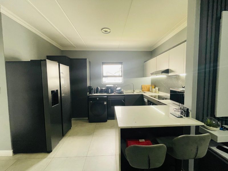Modern kitchen featuring sleek dark and light cabinetry, stone countertops, a breakfast bar, and integrated appliances with contemporary under-cabinet lighting.