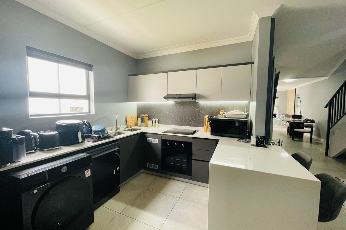 Modern kitchen featuring sleek two-tone cabinetry, stone countertops, integrated oven and hob, and tiled flooring, with an open-plan layout flowing into the living area.