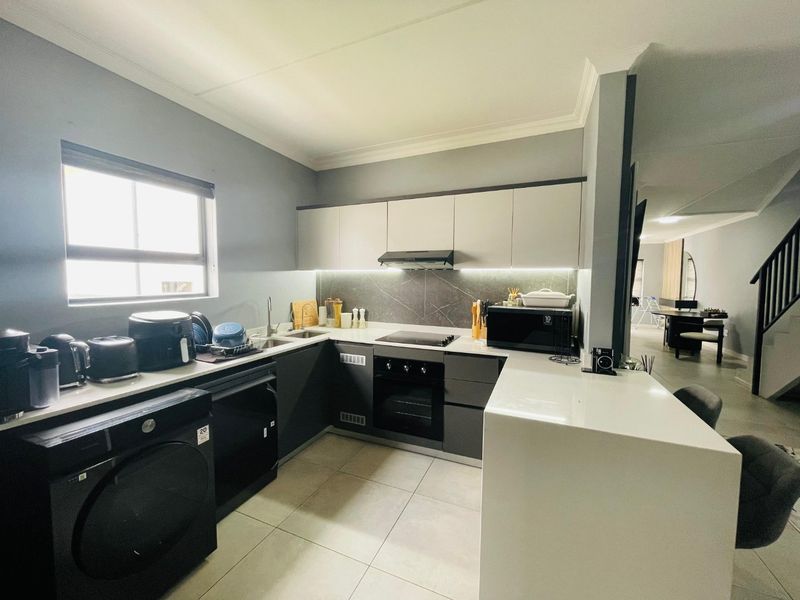 Modern kitchen featuring sleek two-tone cabinetry, stone countertops, integrated oven and hob, and tiled flooring, with an open-plan layout flowing into the living area.