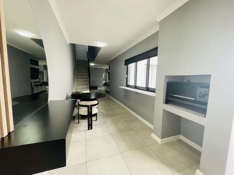 Modern living area featuring neutral grey walls, tiled flooring, a built-in fireplace, and a staircase leading to the upper level.