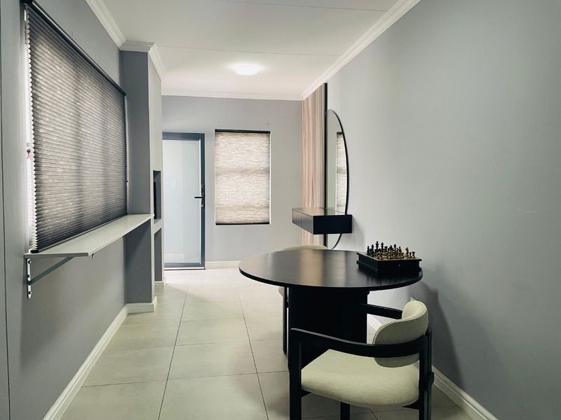 A well-maintained hallway featuring neutral tiled flooring, modern cellular blinds, and a built-in floating shelf, leading towards a glass-panelled exterior door.