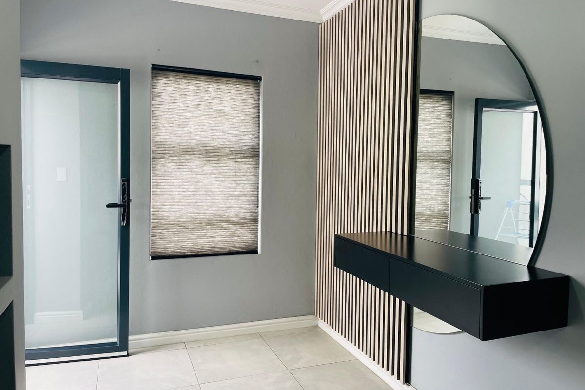 Modern bedroom featuring contemporary slatted timber wall paneling, a floating vanity with a large mirror, tiled flooring, and a frosted glass door.