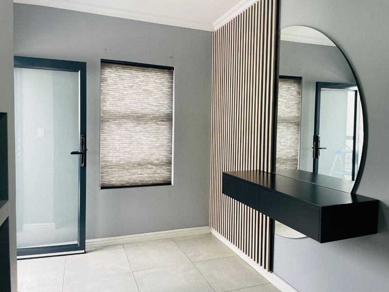 Modern bedroom featuring contemporary slatted timber wall paneling, a floating vanity with a large mirror, tiled flooring, and a frosted glass door.