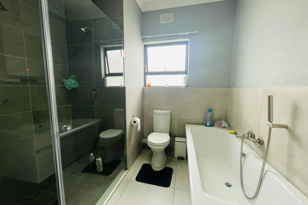 A modern bathroom featuring a glass-enclosed shower, a separate bathtub, and neutral wall and floor tiling.