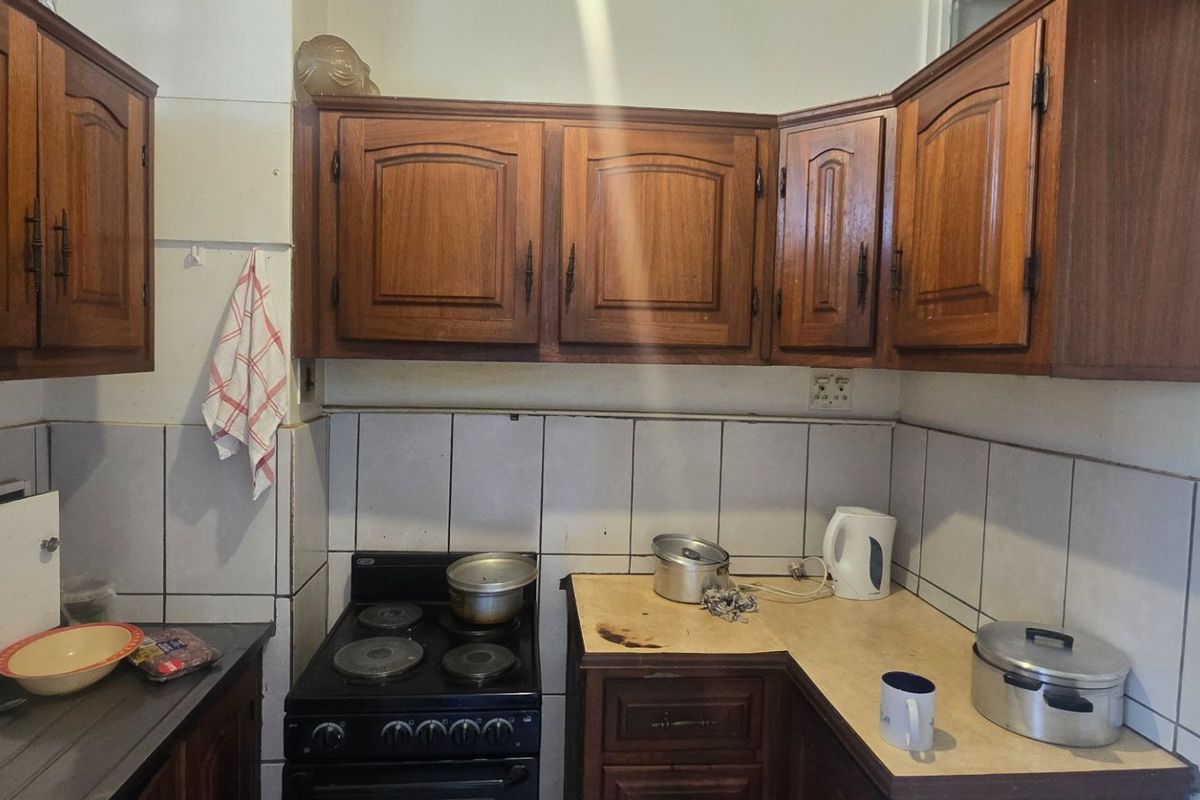 A compact kitchen featuring traditional wooden cabinetry, tiled backsplash, and an electric stove, offering a functional layout with potential for modern updates.