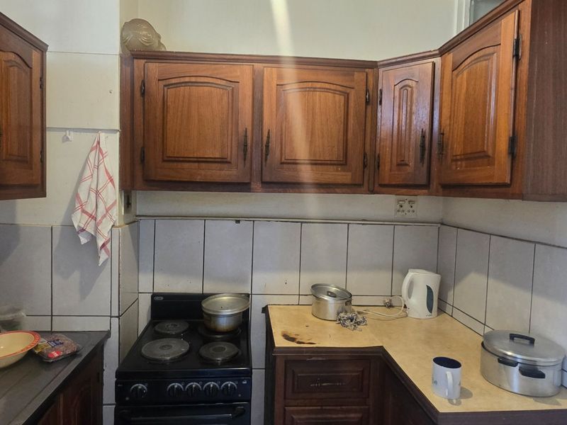 A compact kitchen featuring traditional wooden cabinetry, tiled backsplash, and an electric stove, offering a functional layout with potential for modern updates.