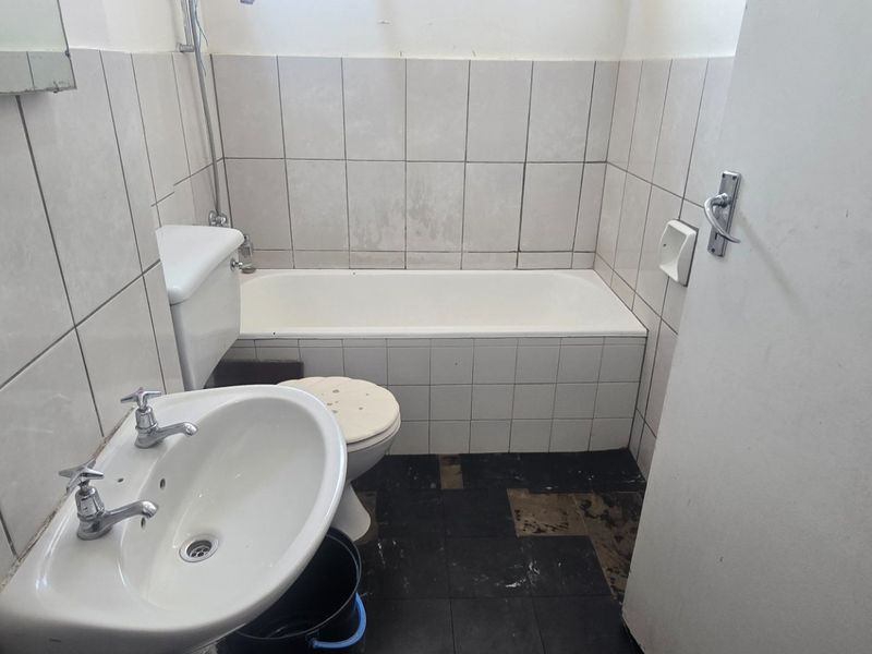 A compact bathroom featuring a standard bathtub, pedestal basin, and toilet, requiring significant renovation and tile repairs to restore functionality and aesthetic appeal.
