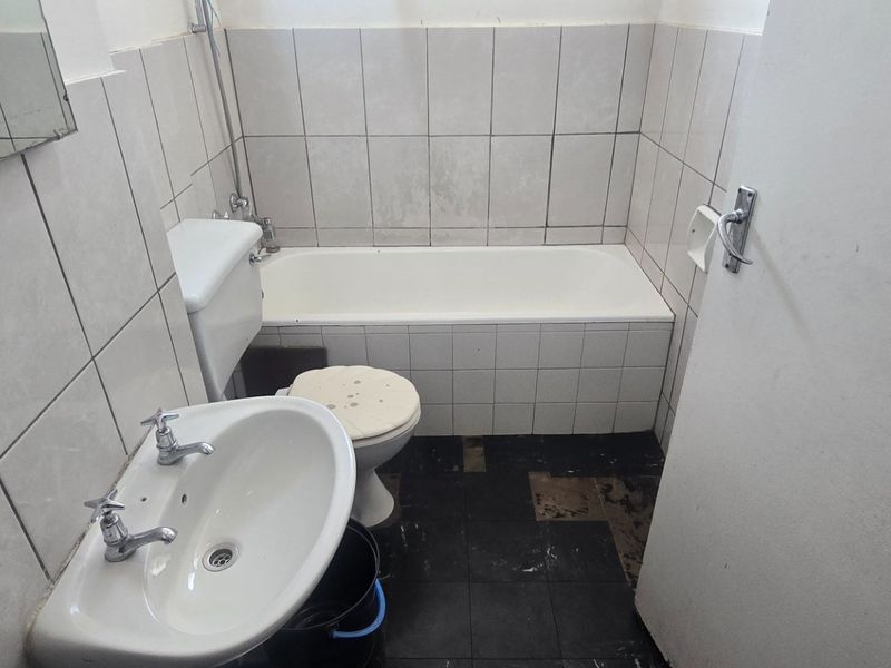 A dated bathroom featuring a bathtub, pedestal basin, and toilet with tiled finishes, requiring renovation and repair to the flooring and fixtures.