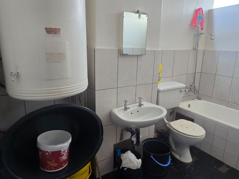 A dated bathroom featuring a pedestal basin, toilet, bathtub, and an exposed electric water heater, requiring significant renovation and modernization of fixtures.