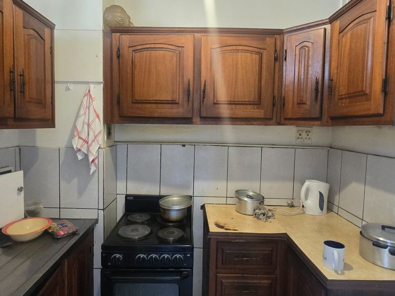 A compact kitchen featuring traditional wooden cabinetry, tiled backsplash, and a built-in electric stove, offering a functional layout with potential for modernization.