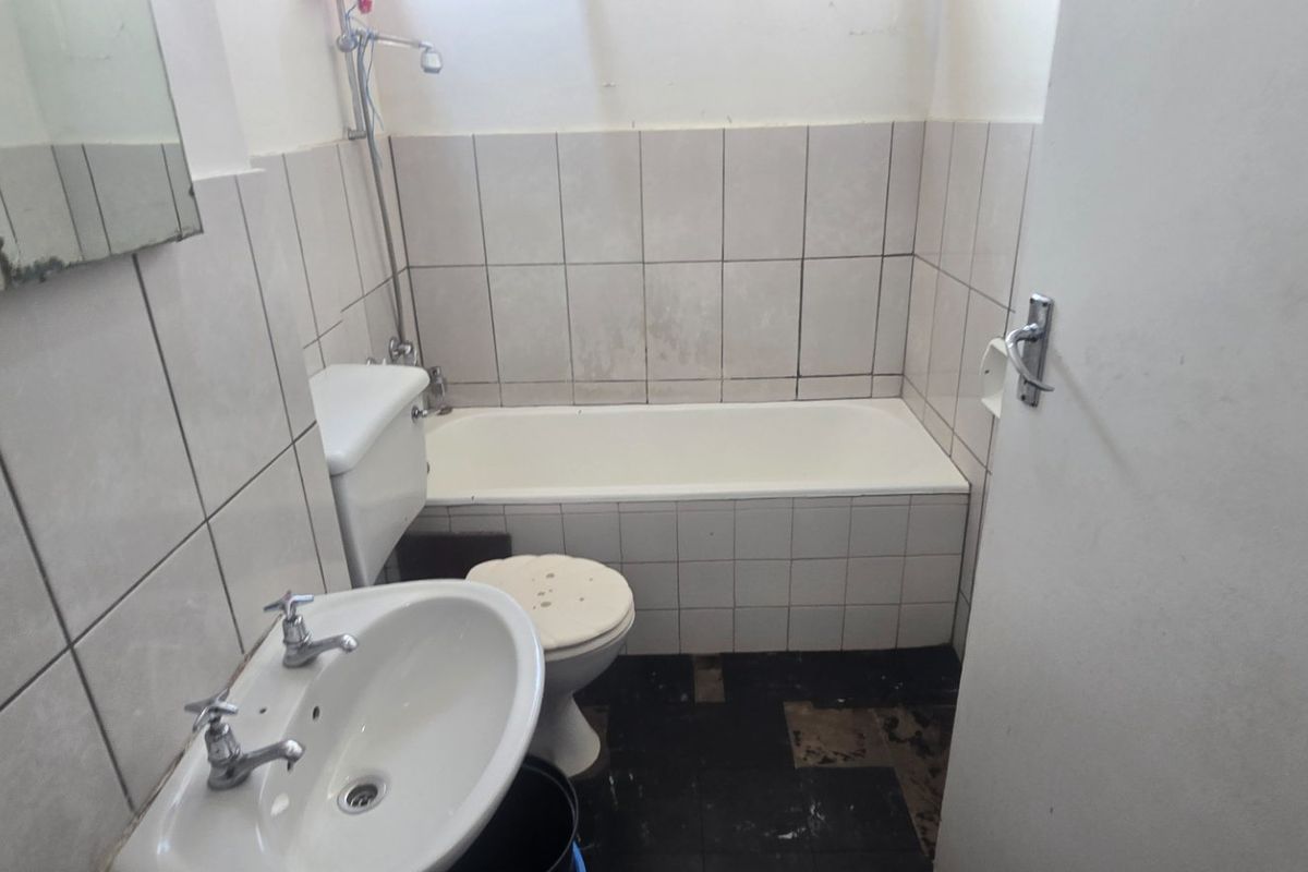 A dated bathroom featuring a standard bathtub, pedestal basin, and toilet, requiring significant renovation and tile replacement to restore functionality and aesthetic appeal.