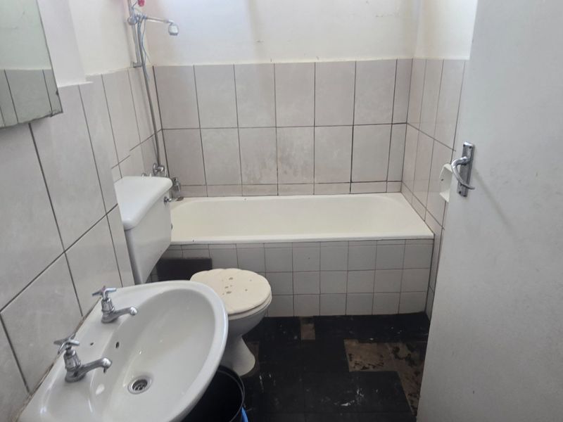 A dated bathroom featuring a standard bathtub, pedestal basin, and toilet, requiring significant renovation and tile replacement to restore functionality and aesthetic appeal.