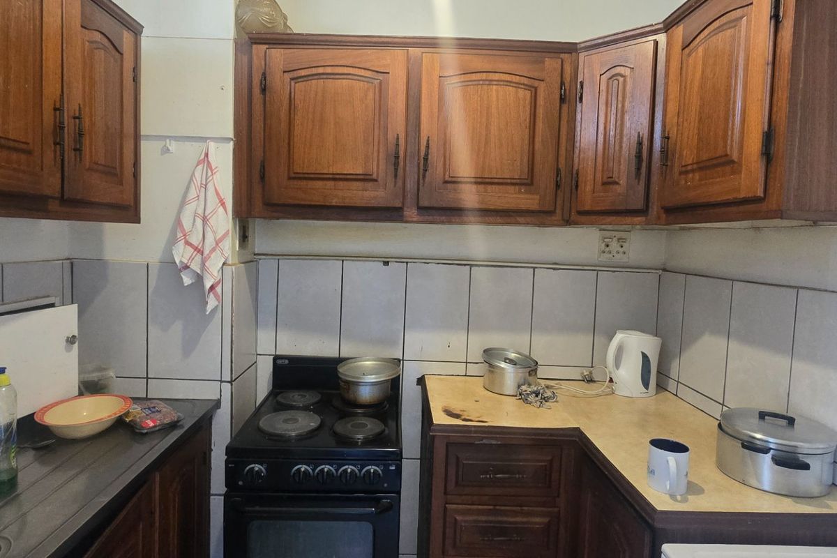 A compact kitchen featuring traditional wooden cabinetry, tiled backsplash, and a built-in electric stove, offering a functional space with potential for modern updates.