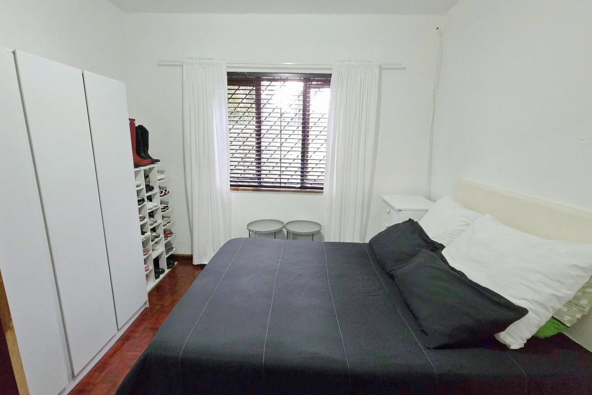 A bedroom featuring wooden flooring, a built-in wardrobe, and a window with blinds, providing a functional and neutral living space.