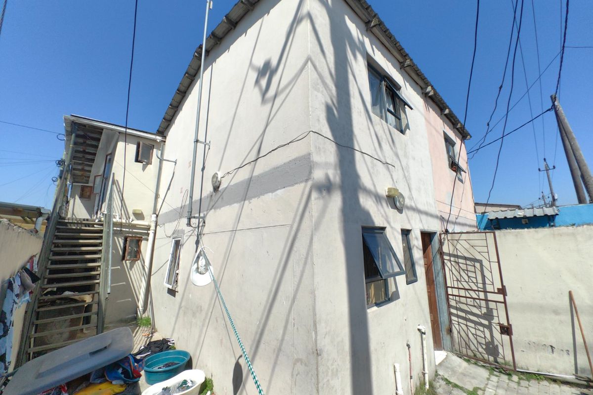 Rear view of a two-story residential building featuring an external staircase, metal security gate, and weathered exterior walls with visible signs of wear.