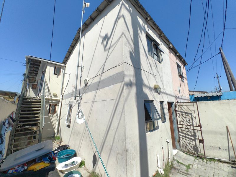 Rear view of a two-story residential building featuring an external staircase, metal security gate, and weathered exterior walls with visible signs of wear.