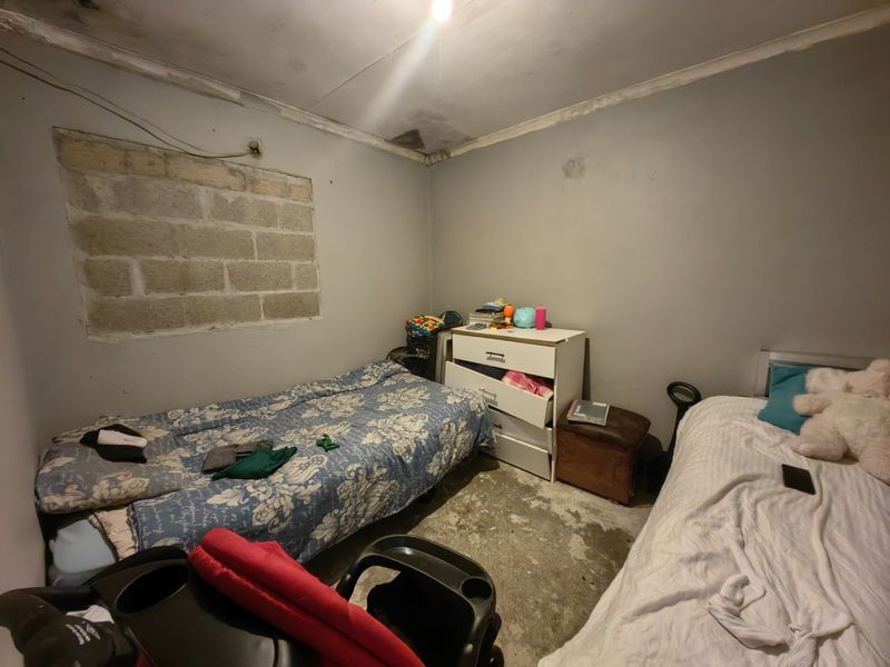 A bedroom featuring unfinished concrete block walls, exposed concrete flooring, and visible ceiling water damage, requiring significant renovation and cosmetic repairs.