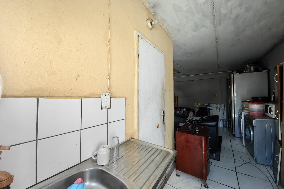 A functional kitchen area featuring a stainless steel sink, tiled splashback, and tiled flooring, currently requiring cosmetic updates and maintenance to the walls and ceiling.