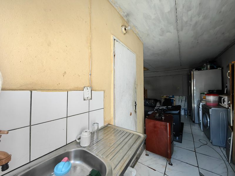 A functional kitchen area featuring a stainless steel sink, tiled splashback, and tiled flooring, currently requiring cosmetic updates and maintenance to the walls and ceiling.