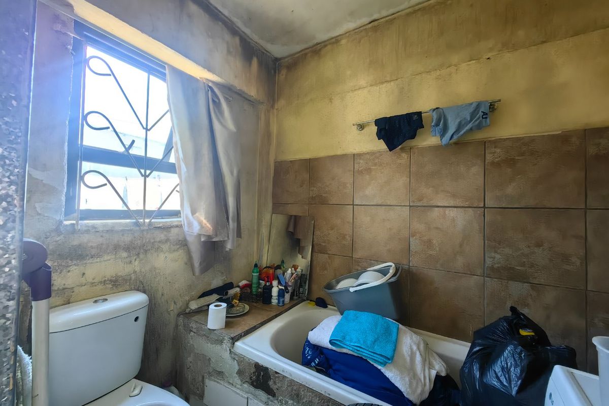 A bathroom requiring significant renovation, featuring a bathtub and toilet, with visible deterioration to the wall finishes and overall structural condition.