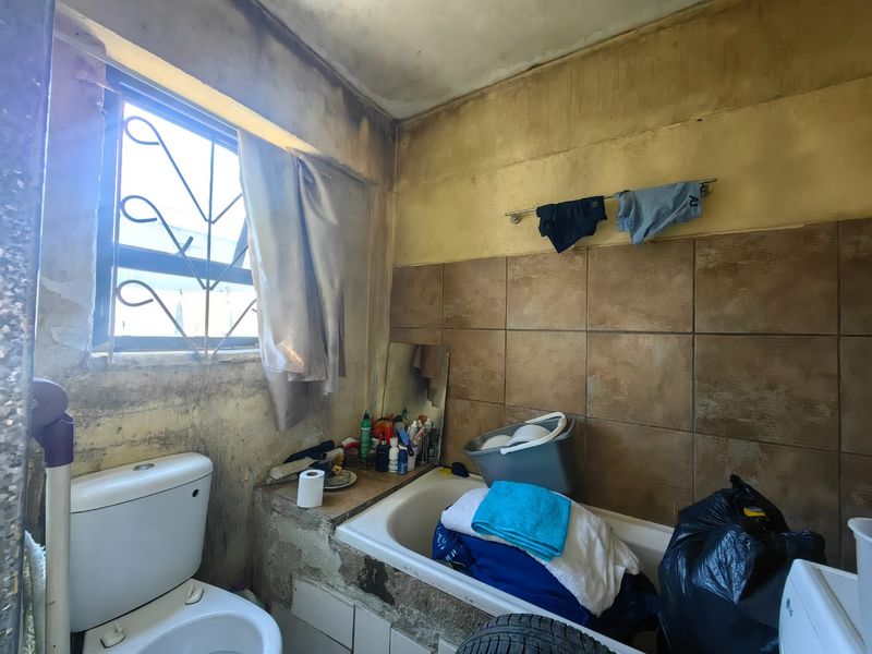A bathroom requiring significant renovation, featuring a bathtub and toilet, with visible deterioration to the wall finishes and overall structural condition.