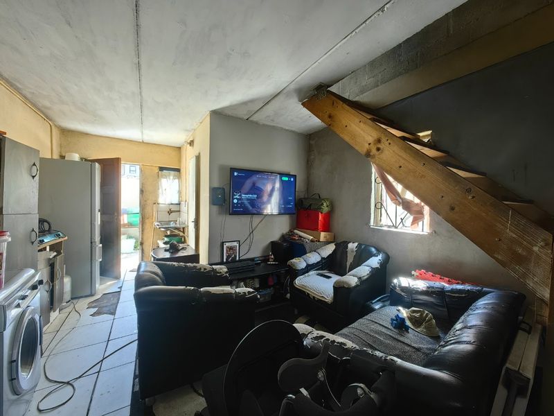 Open plan living area featuring tiled floors, exposed timber staircase, and unfinished wall surfaces, requiring significant renovation to improve the overall aesthetic and condition.