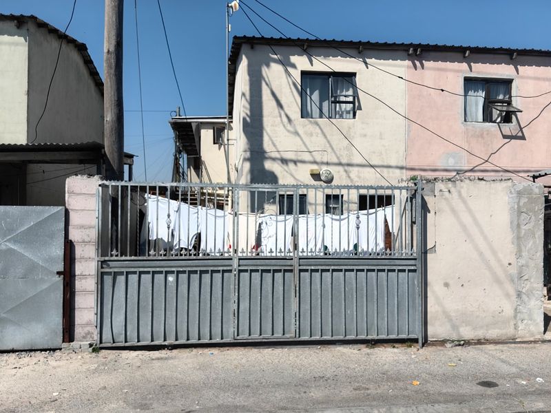 Front view of a residential property featuring a metal security gate and perimeter wall with visible exterior plaster wear.